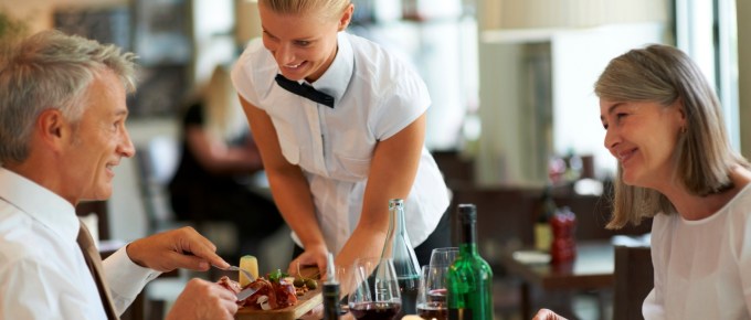 Smiling waitress serving dinner to senior couple at restaurant