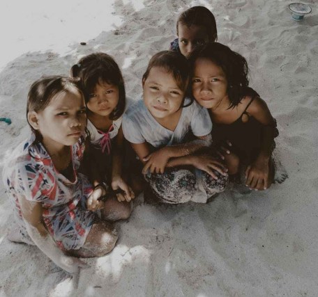 five toddlers sitting on sand
